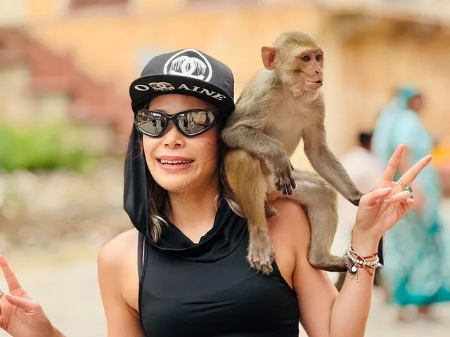 A smiling woman posing with a monkey sitting on her shoulder.