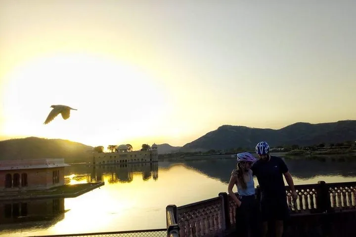 A couple standing by a lake with Jal Mahal in the background.