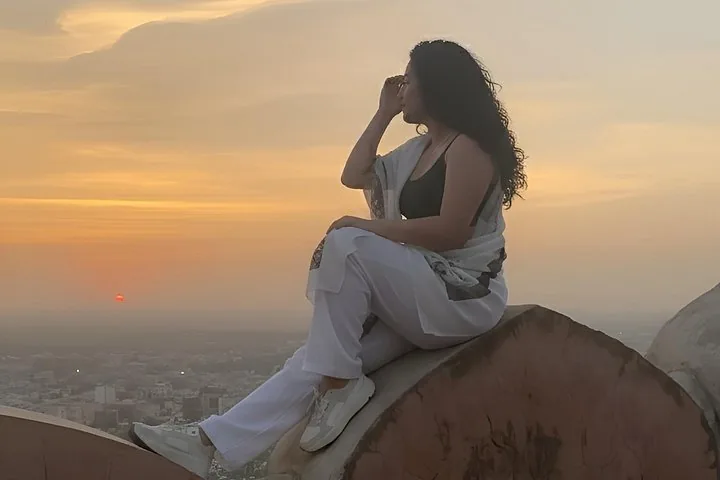 A woman sitting on a wall at Nahargarh Fort during sunset.