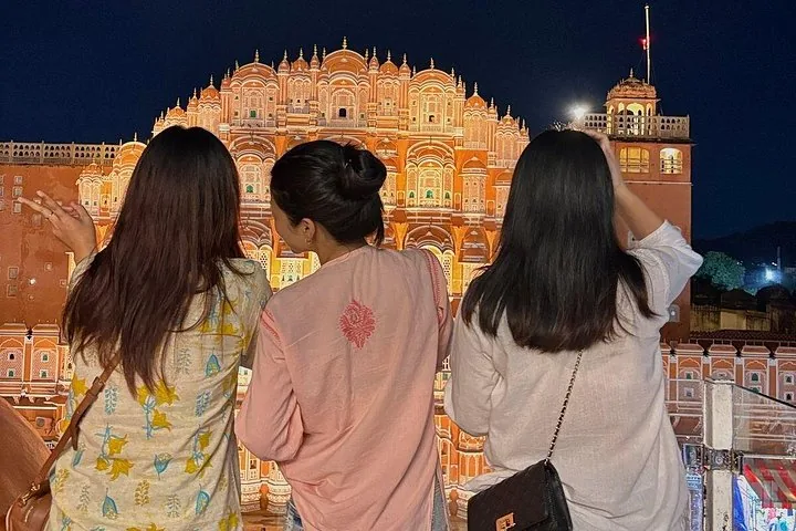 Three women looking at the illuminated Hawa Mahal at night.